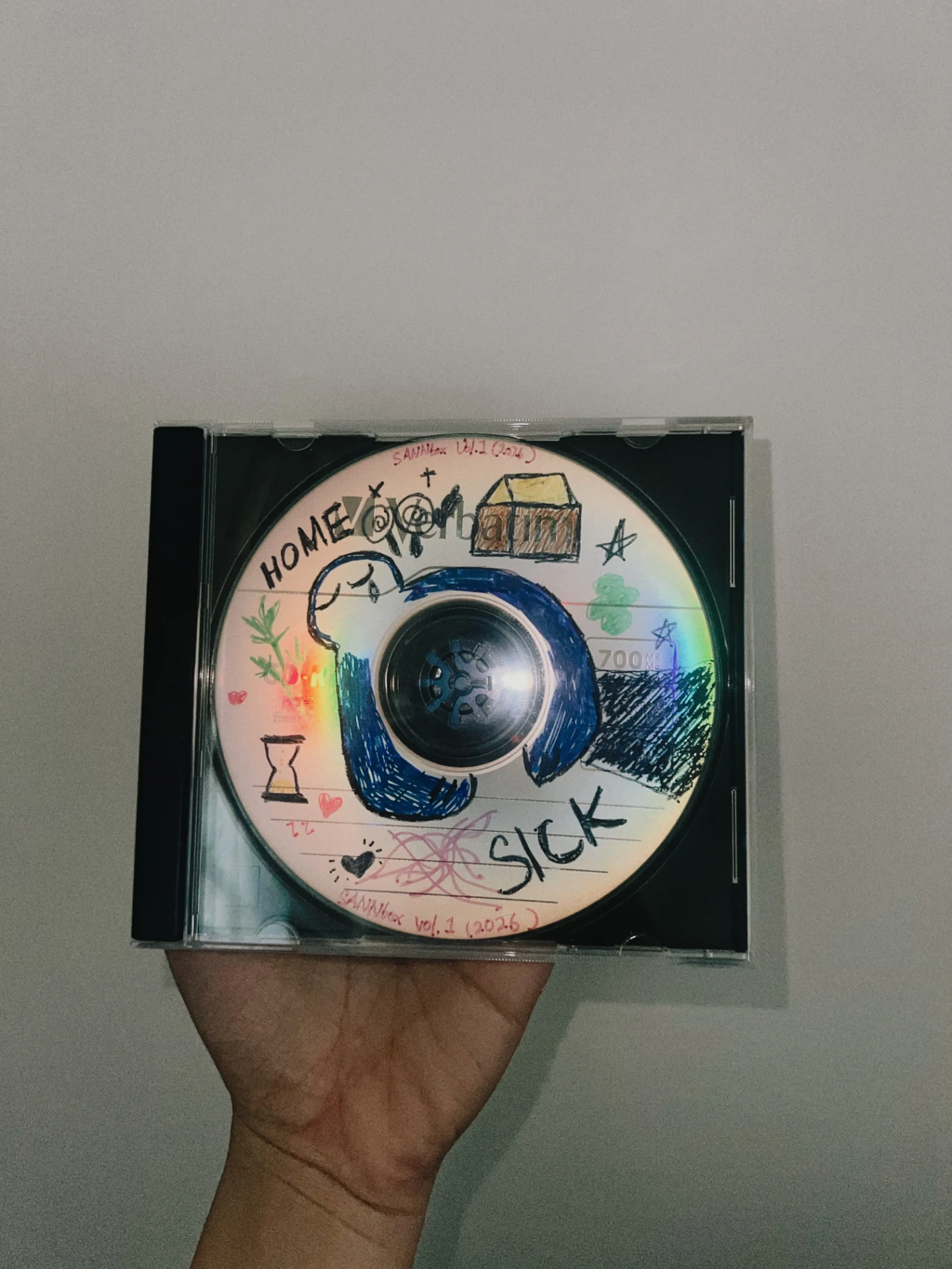 Hand-drawn custom CD-R in a clear jewel case titled “SANNtex Vol.1 (2024)”, decorated with marker doodles of a house, an hourglass, hearts and the words “HOME” and “SICK” — a one-of-one handmade mixtape.